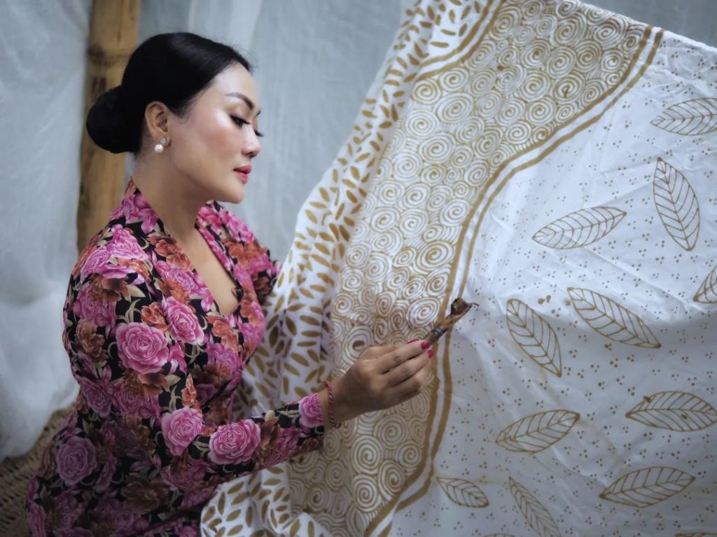 Seorang wanita sedang melukis kain batik sebagai contoh seni rupa tradisional