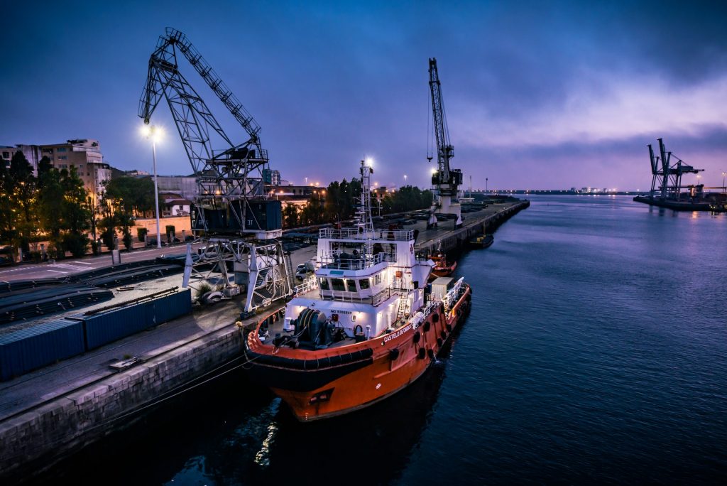 Contoh kegiatan ekonomi maritim perlu kita pahami dengan baik. Yang jelas, ekonomi maritim berbeda dengan kegiatan ekonomi kelautan pada umumnya. Keduanya jelas berbeda baik dari segi pengertian, tujuan, hingga jenis kegiatannya. Namun, orang sering mengartikan keduanya sebagai sesuatu yang sama. Jika kamu ingin mengetahuinya lebih dalam, silahkan simak ulasan berikut ini. Definisi, Manfaat, Serta 10 Contoh Kegiatan Ekonomi Maritim di Indonesia Pada bagian pembuka telah disebutkan bahwa ada perbedaan antara ekonomi maritim dan kelautan. Ekonomi maritim adalah segala aktivitas ekonomi yang terjadi di pesisir laut serta tak lepas dari segala hal yang berkaitan dengan transportasi laut. Sedangkan ekonomi kelautan berarti segala aktivitas perekonomian yang erat hubungannya dengan hasil laut. Mudahnya, ekonomi maritim mencakup semua hal dalam ekonomi kelautan. Dari sini sudah pahamkah kamu perbedaan keduanya? Supaya lebih paham lagi, mari kita simak perbedaannya dari segi tujuan. Ekonomi maritim bertujuan supaya bangsa lebih siap menghadapi persaingan dunia. Selain itu, ekonomi maritim juga memiliki tujuan mengembangkan usaha pembuatan kapal dan meningkatkan armada kapal. Seluruh kegiatannya hampir berlangsung di laut, baik tepi, tengah laut, bahkan tengah samudra. Nah, kalau ekonomi kelautan memiliki tujuan membangun wilayah atau daerah yang ada di sekitar laut. Seluruh kegiatan terpusat agar bisa menghasilkan barang atau jasa. Semua hasil produk memiliki nilai ekonomi. Misal hasil tangkapan ikan oleh nelayan. Secara tak kasat mata, kegiatan maritim baik di tepi atau tengah laut memang tidak menghasilkan produk, contohnya jasa pergudangan laut. Namun secara tak kasat mata kedua aktivitas perekonomian tersebut faktanya tetap menghasilkan produk. Perbedaannya hanya terletak pada lama prosesnya, yakni ekonomi maritim memerlukan waktu lebih panjang serta melibatkan banyak pihak. Supaya memudahkan kamu memahami ekonomi maritim, sebaiknya simak saja beberapa contoh kegiatan ekonomi maritim adalah sebagai berikut: Berikut 10 Contoh Kegiatan Ekonomi Maritim 1. Industri Perkapalan (Pembuatan Kapal Laut) Industri pembuatan kapal laut merupakan salah satu contoh kegiatan ekonomi maritim di Indonesia yang memicu berbagai sektor maritim lain sehingga bisa tumbuh dan menjadi pusat-pusat perekonomian baru. Kedepannya, industri perkapalan atau galangan kapal akan menjelma sebagai industri masa depan terpenting dan paling strategis. Hal ini sangat mungkin terjadi mengingat bahwa Indonesia merupakan negara kepulauan terbesar seantero jagat. Bahkan Indonesia berpotensi sebagai negara maritim yang kuat. Sejak 2018 silam, perkembangan industri perkapalan di Indonesia berjalan cukup signifikan. Hal ini benar adanya mengingat Indonesia adalah sebagai negara kepulauan terbesar di dunia, serta adanya campur tangan Pemerintah dalam pembuatan industri maritim nasional sehingga mampu berkembang. Tujuan pemerintah memperluas produksi perkapalan adalah supaya wilayah yang sulit sekalipun memungkinkan untuk dijangkau dengan mudah. 2. Industri Reparasi Kapal Industri reparasi kapal juga merupakan salah satu contoh kegiatan ekonomi maritim di Indonesia yang mendapat perhatian dari berbagai kalangan. Pasalnya, tujuan dari reparasi itu sendiri adalah bukan sekedar merawat dan memelihara kapal. Lebih dari itu, reparasi kapal adalah suatu proses pemulihan suatu kondisi peralatan atau permesinan yang telah rusak sehingga mengalami penurunan performa. Seperti namanya, reparasi kapal merupakan proses perbaikan atau penggantian bagian-bagian kapal yang sudah tidak layak serta tak memenuhi standar minimal kelayakan untuk digunakan berlayar. Standar kelayakan tersebut berdasarkan peraturan statutory maupun kelas. Pada dasarnya industri reparasi tidak jauh-jauh dari industri galangan kapal atau pembuatan kapal. Dalam praktiknya, industri reparasi kapal melayani perbaikan kapal dan umumnya bergerak berskala besar. 3. Industri Pembuatan Senjata dan Kapal Perang Contoh kegiatan ekonomi maritim di Indonesia selanjutnya adalah industri pembuatan senjata dan kapal perang. Dulu persenjataan negara kita sangat bergantung dari produk impor. Hal ini karena orang Indonesia masih minim pengetahuan dan anggaran dana. Namun, kini tidak lagi. Pada 5 Desember 2021 silam PT PAL telah meluncurkan kapal perang hasil karya murni anak bangsa. Kapal perang tersebut diberi nama Kapal Cepat Rudal (KCR). Dimensi kapal yakni 60 meter x 8,10 meter x 4,85 meter. Adapun daya muat kapal kurang lebih 450 ton hingga 500 ton. Kapal perang juga memiliki persenjataan yang mampu mendeteksi target di udara, permukaan, hingga bawah laut. Ini karena KCR dipersenjatai senapan kapal 57 Bofors Shipborne gun 20 mm dan Surface to Surface Missile (SSM) Exocet 40 mm. Menilik dari kemajuan tersebut, apakah kamu bangga menjadi orang Indonesia yang sukses membikin senjata dan kapal perang sendiri? 4. Jasa Pergudangan Laut Jasa pergudangan laut merupakan contoh kegiatan ekonomi maritim sekaligus sebagai pemberi kontribusi dalam devisa negara. Dalam ekonomi maritim, keberadaan jasa ini cukup penting karena memungkinkan mode transportasi untuk menyimpan barang di sekitar wilayah pelabuhan. Jasa pergudangan laut merupakan salah satu cara untuk mengoptimalkan tol laut. 5. Terminal Peti Kemas Terminal peti kemas merupakan fasilitas untuk memindahkan kargo peti kemas sebelum mengirimnya. Kita bisa menyebutnya dengan bongkar muat peti kemas. Fasilitas terminal peti kemas yang dimaksud adalah dermaga (pelabuhan), lapangan penumpukan (untuk mengumpulkan, menyimpan, atau menumpuk peti kemas dengan muatan diterima), serta container yard (daerah pelabuhan untuk menimbun petikemas FCL yang nantinya akan dimuat ataupun dibongkar dari kapal). Jadi, terminal petikemas merupakan tempat sementara pengumpulan peti kemas dari hinterland atau pelabuhan lain sebelum diangkut dan dikirim ke tempat tujuan atau terminal peti kemas yang lebih besar lagi. Jenis peti kemas antara lain adalah dry cargo container, reefer container, bulk container, open side container, soft top container, open top-open side container, tank container, dan flat rack container. 6. Jasa Navigasi Kapal Tahukah kamu apa itu jasa navigasi kapal? Dalam contoh kegiatan ekonomi maritim di Indonesia, pengertian jasa navigasi kapal adalah jasa kegiatan untuk membantu awak kapal dalam berkomunikasi, baik dalam satu kapal ataupun antar kapal. Keberadaan jasa tidak boleh dipandang sebelah mata. Mereka akan membantu proses berlayarnya kapal sekaligus menentukan arah berlayar. Hal ini sesuai dengan fungsi navigasi itu sendiri yakni sebagai penentu kedudukan dan arah perjalanan di medan laju sesungguhnya. 7. Tol Laut Seperti tol pada umumnya, pembuatan tol laut erat kaitannya dengan kelancaran jalur pelayaran dan pengangkutan logistik di tanah air. Tol laut difungsikan untuk mengatur lalu lintas bebas hambatan bagi kapal-kapal yang berlayar di perairan Nusantara. Salah satu contoh kegiatan ekonomi maritim di Indonesia berupa tol ini pada prinsipnya adalah melakukan aktivitas pelayaran secara rutin termasuk menjadwalkan pelayaran tersebut dari barat sampai ujung timur wilayah Indonesia untuk memperkuat jalur pelayaran dan logistik. Adanya tol laut diharapkan bisa menjaga ketersediaan barang pokok dan penting di kawasan daerah tertinggal, terpencil, terluar, dan perbatasan (3TP). Program ini telah ada sejak 2015 silam. Hingga saat ini telah ada setidaknya 33 trayek tol laut nasional dari Aceh hingga Papua. Program nasional dari Presiden Jokowi ini terealisasi karena latar belakang adanya disparitas harga yang cukup signifikan antara wilayah barat dan timur. Intinya, pengangkutan logistik kelautan Indonesia ini bertujuan untuk menghubungkan berbagai pelabuhan besar di wilayah Nusantara. 8. Aktivitas Perekonomian Pelabuhan Satu lagi contoh kegiatan ekonomi maritim di Indonesia yaitu aktivitas perekonomian pelabuhan. Umumnya ada 5 aktivitas ekonomi pokok yang terjadi di pelabuhan. Aktivitas ekonomi tersebut meliputi pelayanan kapal, handling bongkar muat, embarkasi dan debarkasi penumpang. Pariwisata dan ekonomi tumbuh bersama. Artinya, kedua variabel tersebut tidak bisa terpisahkan. Salah satu yang memegang andil pertumbuhan ekonomi dan pariwisata adalah kehadiran pelabuhan. Misalnya pelabuhan penyeberangan Ulee Lheue, Aceh. Seluruh potensi aktivitas ekonomi tanpa terkecuali telah tumbuh dan berkembang dari pelabuhan tersebut. Sementara itu, dari aspek pariwisatanya, pelabuhan Ulee Lheue memiliki ruang hijau dengan background pesona keindahan alam sehingga siapapun yang datang ke pelabuhan bisa menikmatinya. Tak jarang beberapa pengunjung memanfaatkan ruang hijau di pelabuhan sebagai tempat piknik keluarga. Menilik dari kondisi tersebut, tidak menutup kemungkinan jika kedepannya tercipta potensi pengembangan kuliner dengan cita rasa masakan khas Aceh. Bahkan tidak menutup kemungkinan mulai menjadi incaran investor. 9. Industri Logistik Akomodasi Pengiriman Barang Lewat Jalur Laut Transportasi laut lebih hemat biaya. Apalagi bisa diandalkan sebagai sarana pengangkutan segala jenis produk dalam jarak jauh, misal lintas pulau. Bahkan memudahkan pengangkutan barang dengan volume besar ketimbang mengirimnya lewat jalur udara maupun darat. Transportasi laut juga tak perlu khawatir macet. Namun, bukan berarti bebas macet. Lalu lintas di jalur strategis misalnya wilayah selat di Indonesia. Meskipun demikian, ini masih menjadi keunggulan menggunakan transportasi laut sehingga jasa industri lebih memilih akomodasi via laut. Sebagai contoh kegiatan ekonomi maritim di Indonesia, fakta di lapangan membuktikan bahwa transportasi laut dan maritim begitu strategis untuk kegiatan ekspor impor. Inilah mengapa kota-kota yang berada tak jauh dari pelabuhan bisa tumbuh dan berkembang menjadi daerah yang produktif. 10. Jasa Penyeberangan Antar Pulau Antar Negara Jasa penyeberangan antar pulau antar negara juga termasuk contoh kegiatan ekonomi maritim karena segala aktivitasnya berada dari satu pelabuhan ke pelabuhan lain dengan menggunakan transportasi laut. Indonesia menerapkan ekonomi maritim karena kaya akan pulau-pulau baik besar maupun kecil serta memiliki wilayah laut yang terbilang amat luas. Dari 10 contoh kegiatan ekonomi maritim dalam ulasan tadi, manakah yang menurutmu harus terus dikembangkan? Pada dasarnya, pengupayaan dan pengembangan seluruh aktivitas ekonomi dalam ulasan tadi tidak boleh sampai berhenti di tempat. Maka dari itu, tak salah apabila Pemerintah terus menerus mengupayakannya. Secara nyata, pemerintah telah melakukan upaya pengembangan ekonomi maritim meliputi: Membuat perubahan paradigma sehingga kegiatan ekonomi kelautan bisa berkembang. Jadi, pembangunan darat dan laut bisa berjalan seimbang. Mengoptimalkan pembangunan infrastruktur demi mendukung perkembangan ekonomi kelautan Indonesia. Supaya tercipta ketertiban lalu lintas air laut, maka pemerintah menegakkan aturan kemaritiman. Aturan ini sebagai antisipasi bila ada kapal dari negara lain melintas di perairan Indonesia. Dari 10 contoh kegiatan ekonomi maritim dalam ulasan tadi, pasti membutuhkan adanya kebijakan ekonomi maritim, dan pemerintah telah berupaya penuh menerapkannya. Hingga saat ini kita harus berbangga hati karena telah memiliki kemandirian untuk bisa memenuhi kebutuhan armada kapal. Apakah kamu memiliki gagasan lain untuk mengembangkan kegiatan ekonomi kemaritiman di Indonesia